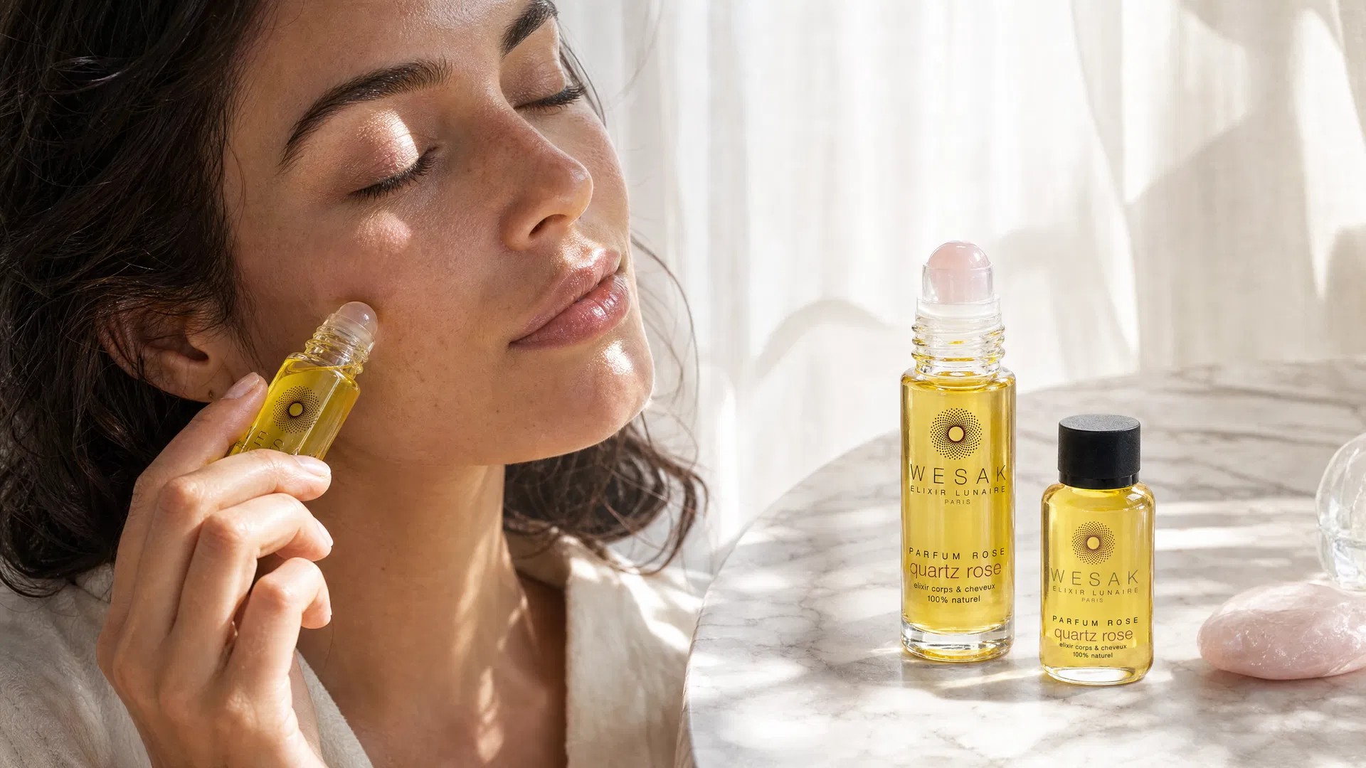 Roll-on en quartz rose Wesak Paris sur marbre blanc entouré de pétales de rose et de cristaux bruts - guide débutant massage facial