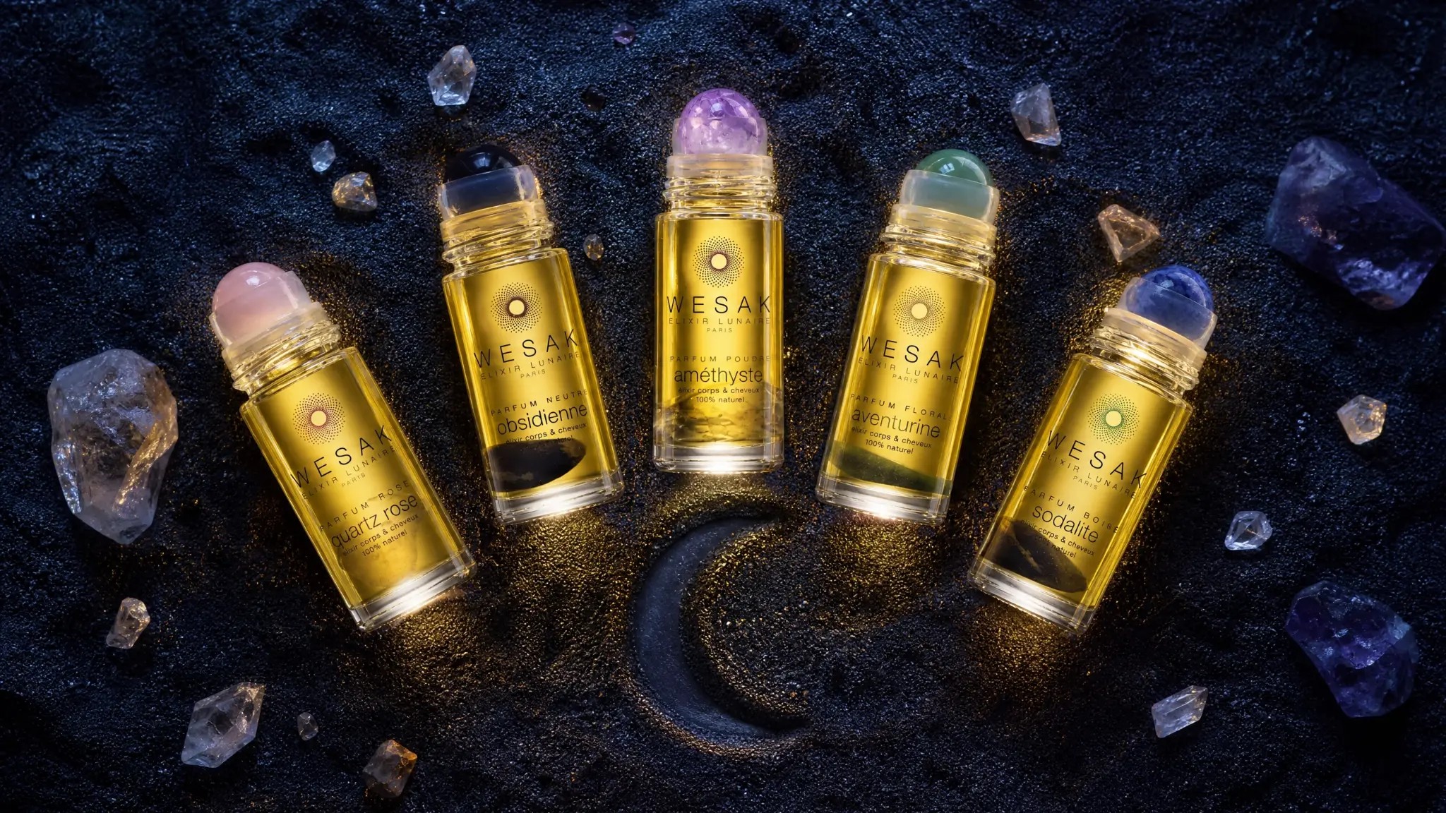 Les 5 élixirs lunaires Wesak Paris quartz rose obsidienne améthyste aventurine sodalite en arc sur sable volcanique noir avec croissant de lune et cristaux bruts - rituel beauté lunaire